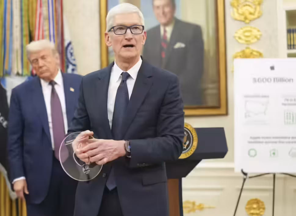 Tim Cook, wearing a dark suit and glasses, holds a clear disc-shaped award while standing at a podium with the Seal of the President of the United States. Donald Trump stands behind him to the left, and a portrait hangs on the wall behind Cook. An easel to the right displays a poster with the text "$600 Billion."