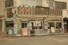 A restaurant storefront has a pale green facade with Japanese signage and a bicycle parked outside. Signs read "手包み餃子" (handmade dumplings), "餃子アイス" (dumpling ice cream), "地酒" (local sake), "日本酒" (Japanese sake), "焼酎" (shochu), "ハイボール" (highball), and "生ビール" (draft beer). A large sign reads "肉汁餃子製作所 タンタタン酒場" (Juicy Dumpling Factory Tantatan Tavern). A sign in front of the entrance reads "持帰り餃子" (takeout dumplings). A white curtain with black writing hangs in the doorway. A sandwich board advertises highballs for 190 yen.