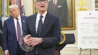 Tim Cook, wearing a dark suit and glasses, holds a clear disc-shaped award while standing at a podium with the Seal of the President of the United States. Donald Trump stands behind him to the left, and a portrait hangs on the wall behind Cook. An easel to the right displays a poster with the text "$600 Billion."