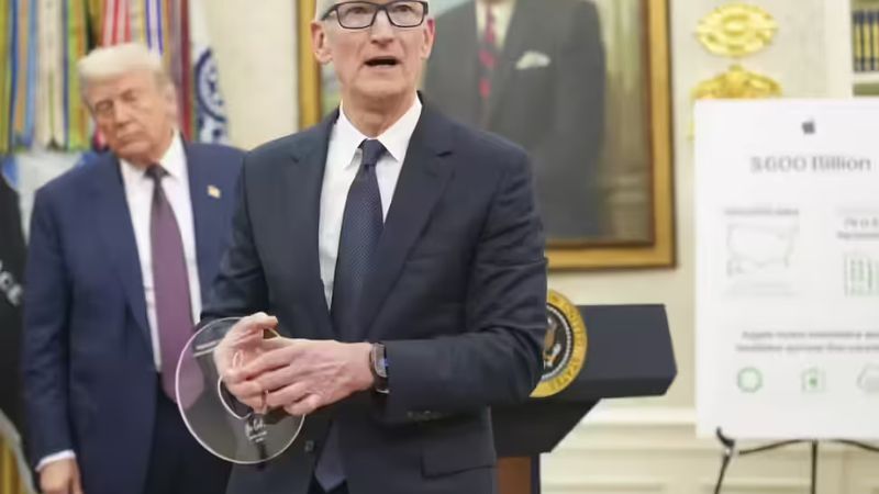 Tim Cook, wearing a dark suit and glasses, holds a clear disc-shaped award while standing at a podium with the Seal of the President of the United States. Donald Trump stands behind him to the left, and a portrait hangs on the wall behind Cook. An easel to the right displays a poster with the text "$600 Billion."
